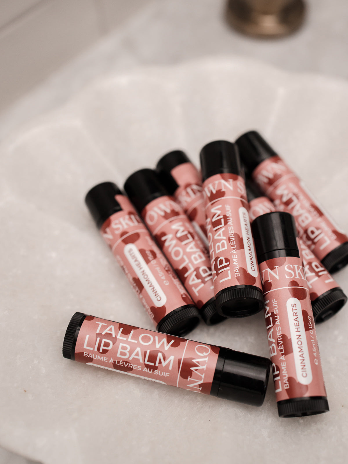 Multiple cinnamon hearts limited edition OWN SKIN CO. tallow lip balms on a white surface