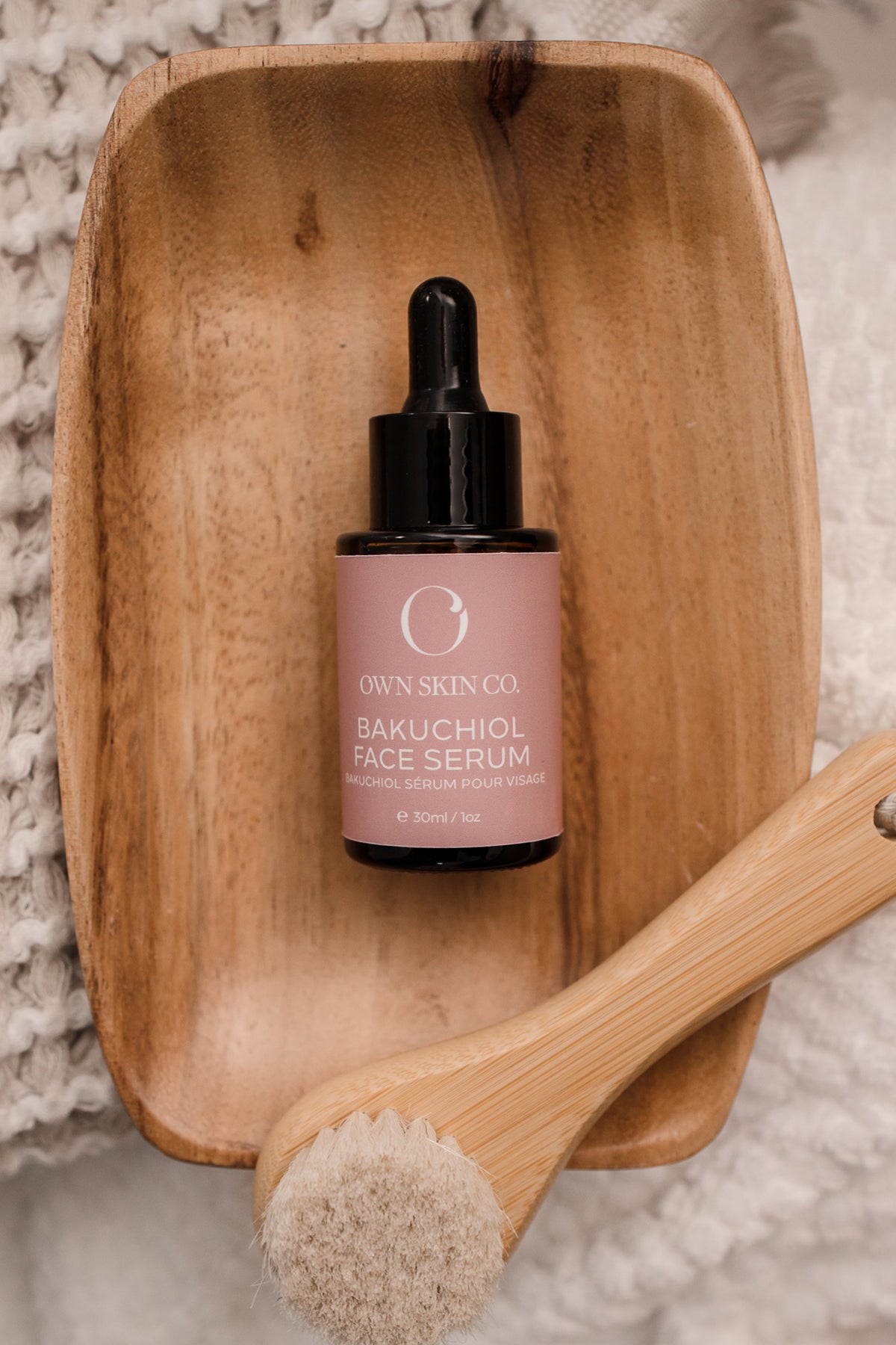 A bakuchiol Face serum with a pink label on a little wooden tray with a bamboo face dry brush laying across