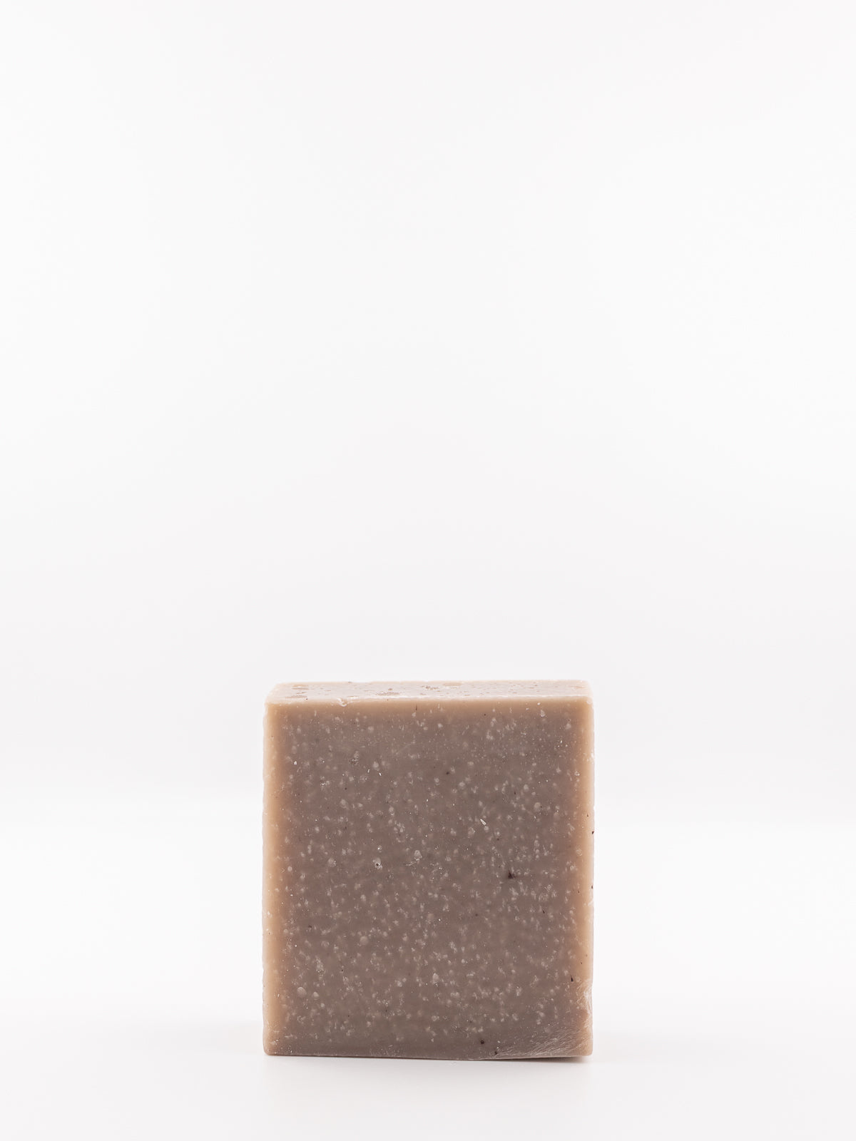 A single square bar of OWN SKIN CO.'s rustic spice hand and body soap with a speckled taupe-brown texture, standing upright against a seamless white background.