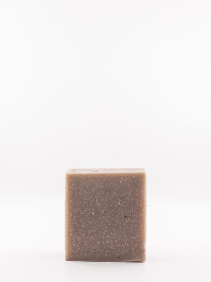 A single square bar of OWN SKIN CO.'s rustic spice hand and body soap with a speckled taupe-brown texture, standing upright against a seamless white background.
