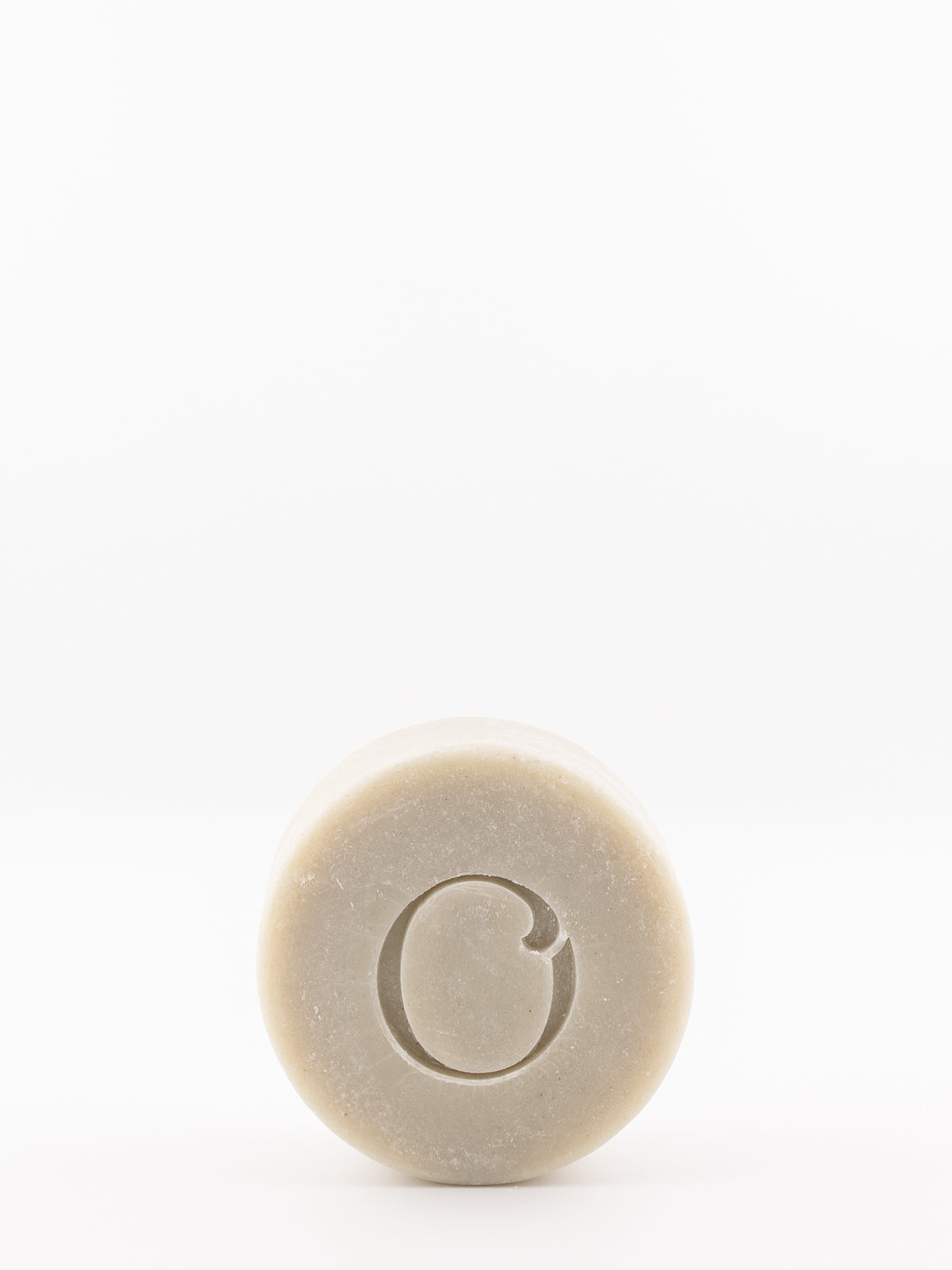 A solid shave bar from own skin co with a carved letter 'O' in the center, shown against a plain white background.