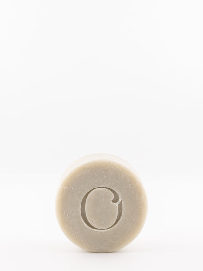 A solid shave bar from own skin co with a carved letter 'O' in the center, shown against a plain white background.