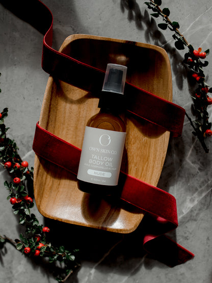 Bottle of natural beef tallow body oil on a wooden tray with a red ribbon, surrounded by greenery for christmas 