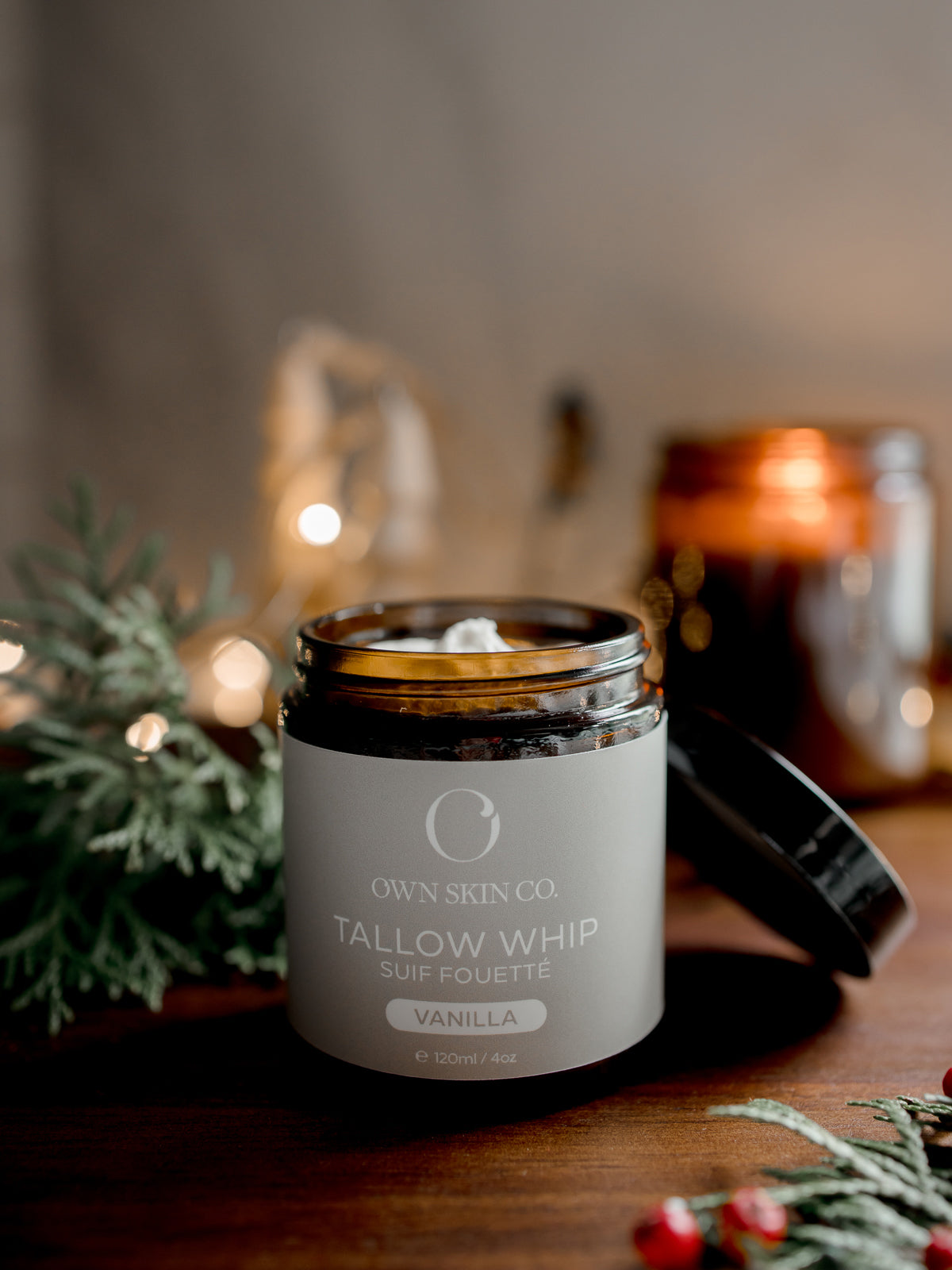 Tallow whip container with 'OWN SKIN CO.' branding on a wooden surface with blurred background