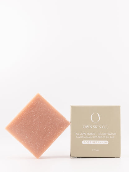 A rose-colored hand and body wash bar with fine glitter stands next to its beige packaging box on a clean white background. The box is labeled 'OWN SKIN CO.