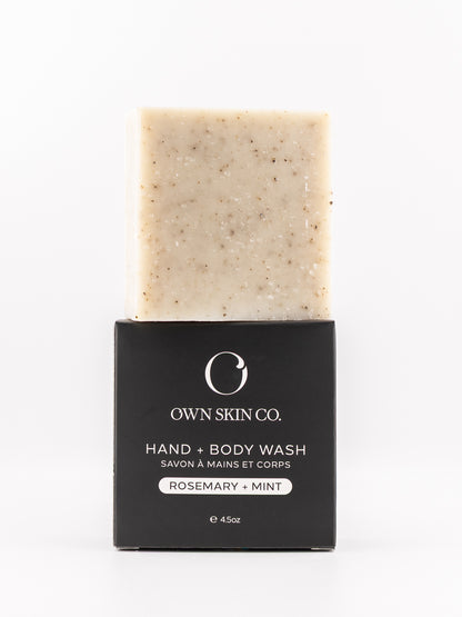 A bar of Own Skin Co. Hand & Body Wash with rosemary and mint, showing the beige speckled soap bar above its black cardboard packaging on a white background.
