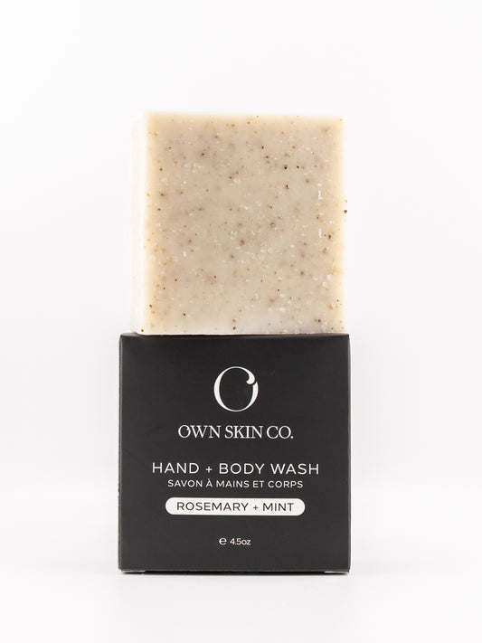 A bar of Own Skin Co. Hand & Body Wash with rosemary and mint, showing the beige speckled soap bar above its black cardboard packaging on a white background.