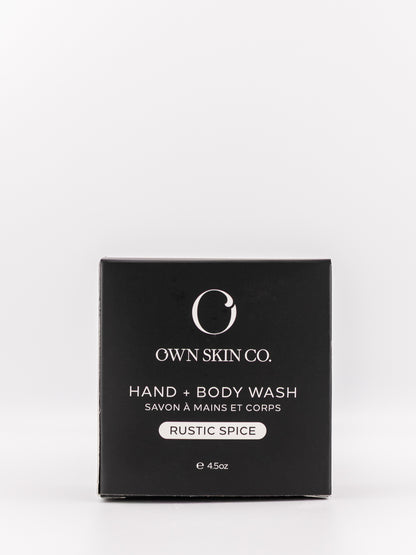 Own Skin Co. Hand + Body Wash in 'Rustic Spice' scent, shown in its black rectangular packaging box against a light gray background.