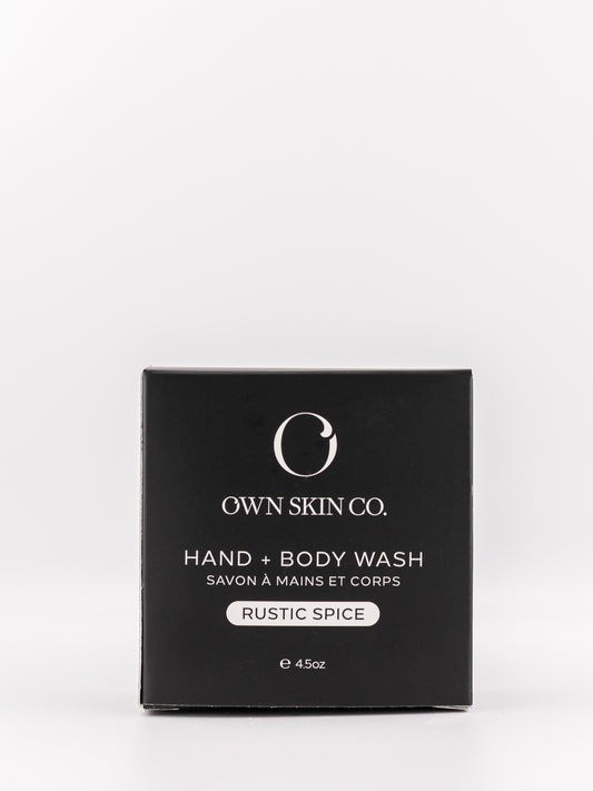 Own Skin Co. Hand + Body Wash in 'Rustic Spice' scent, shown in its black rectangular packaging box against a light gray background.